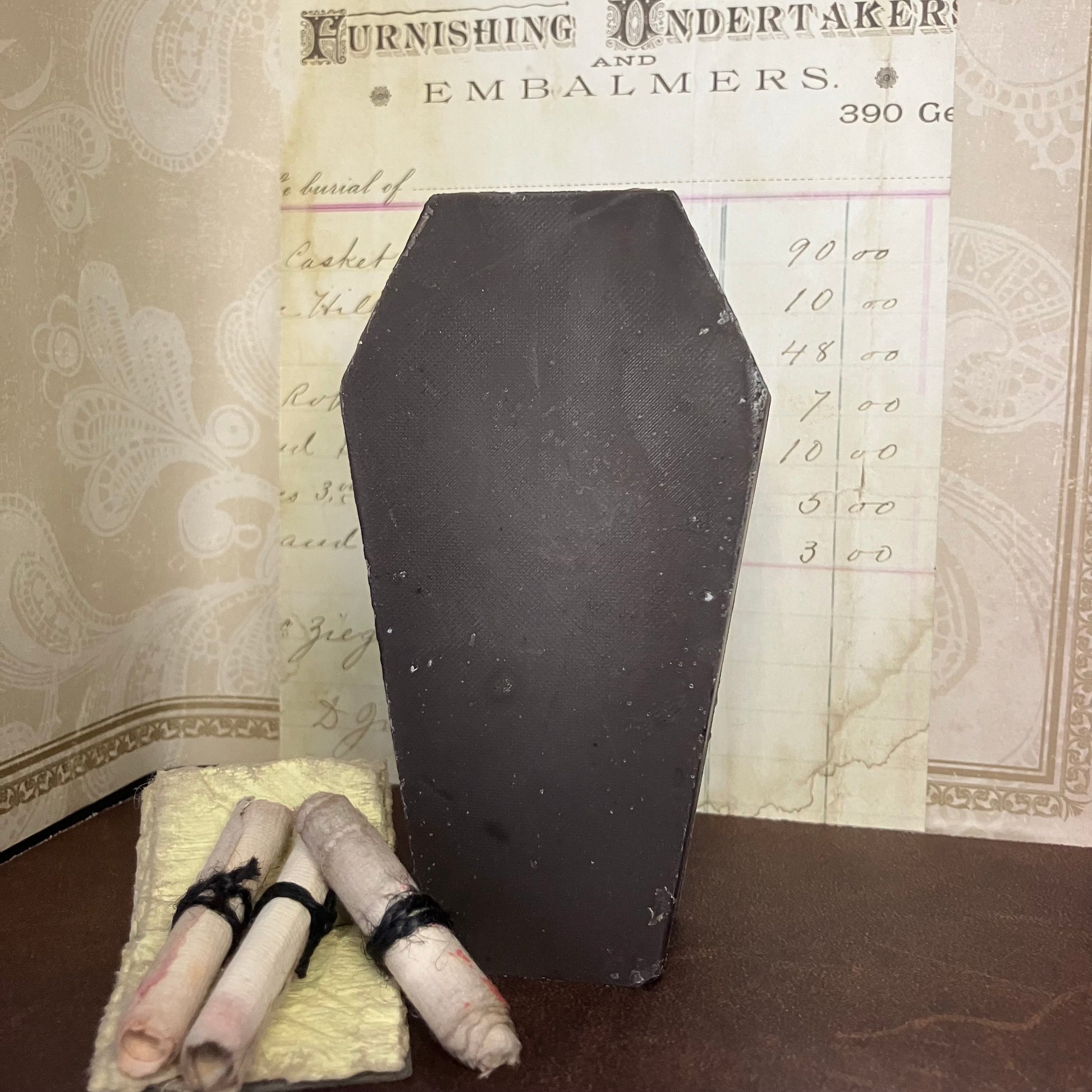 black coffin soap with rolled-up documents on a surface, with an old document in the background.
