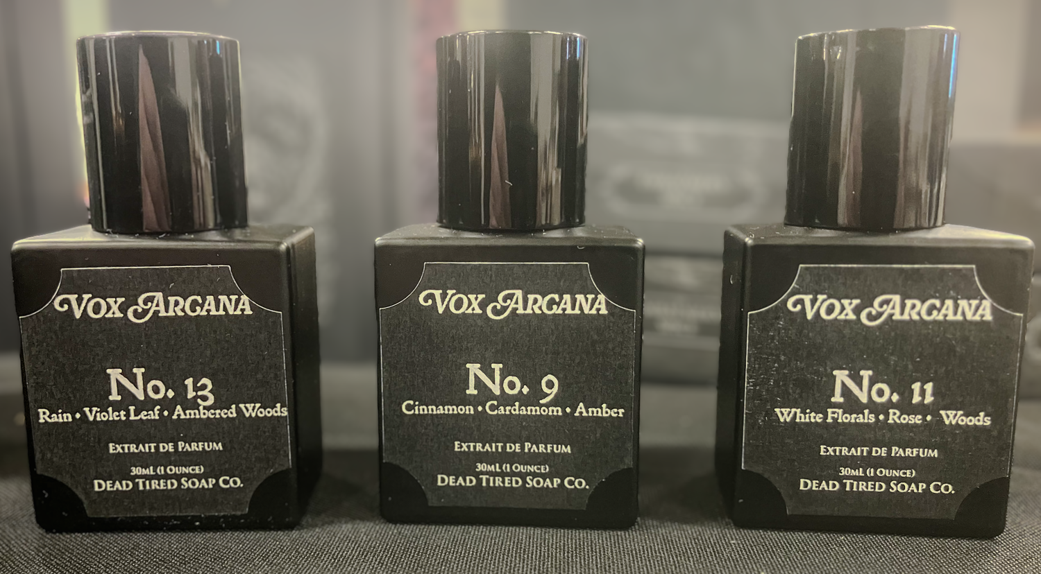 Three Vox Arcana perfume bottles on a gray surface with a blurred background