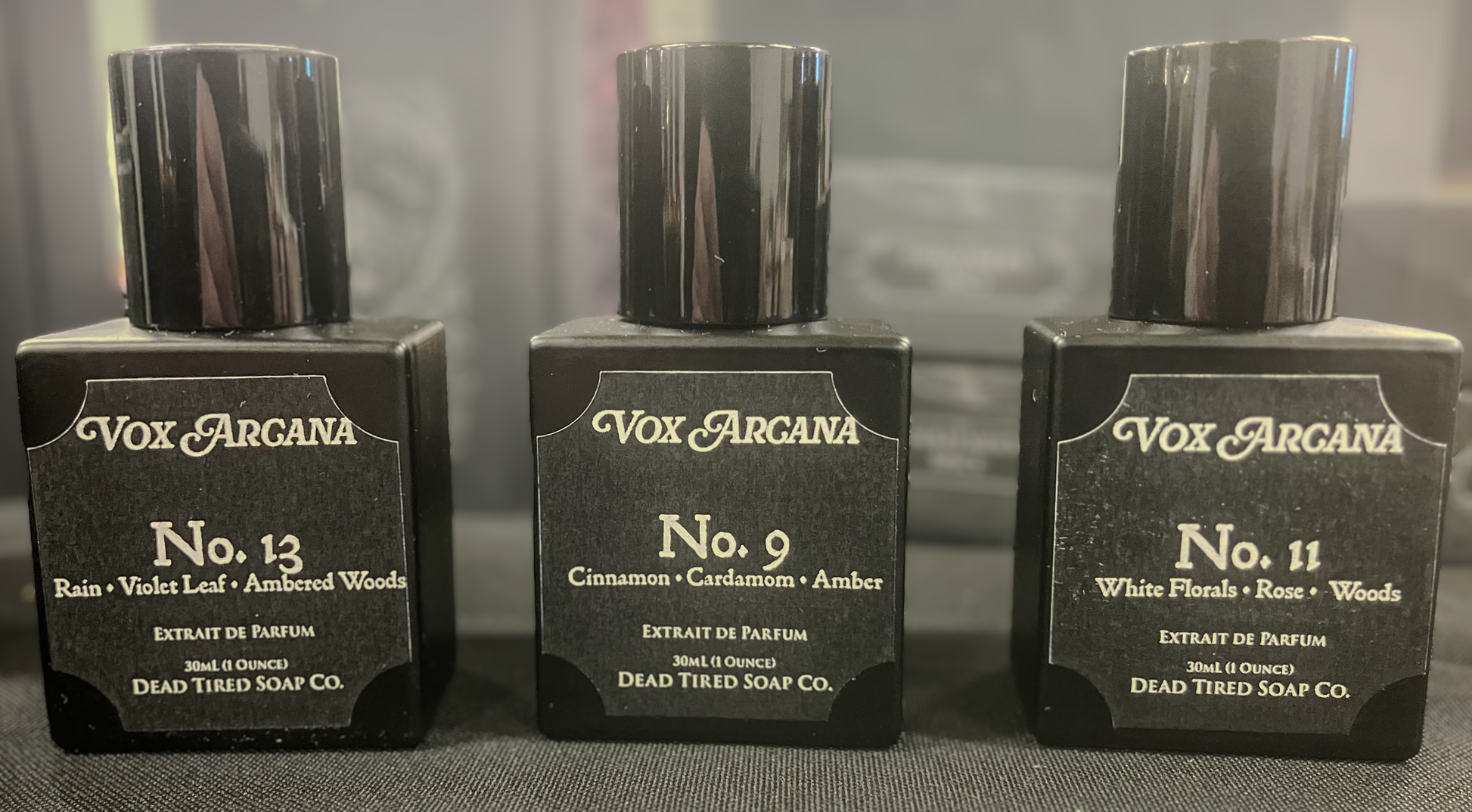 Three Vox Arcana perfume bottles on a gray surface with a blurred background